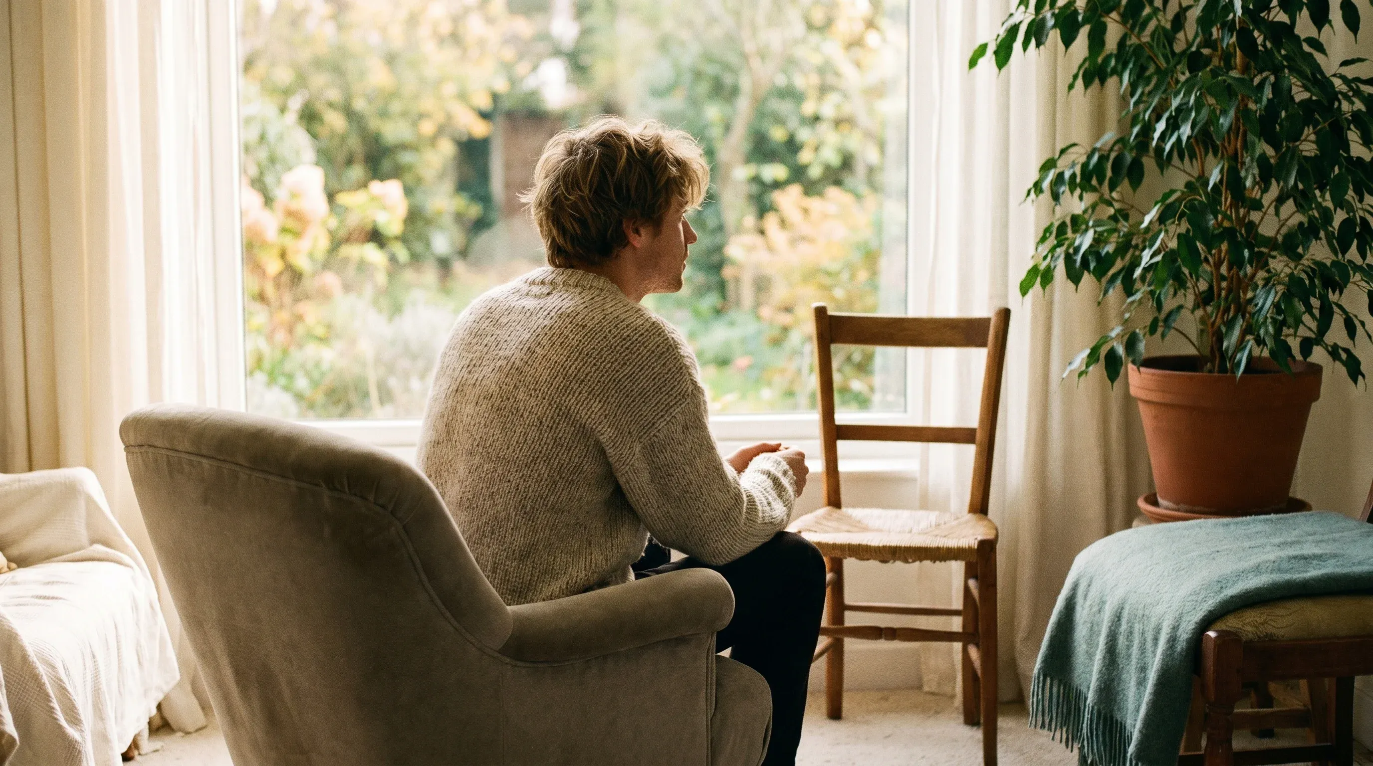 Eine Person sitzt nachdenklich am Fenster, daneben ein leerer Stuhl