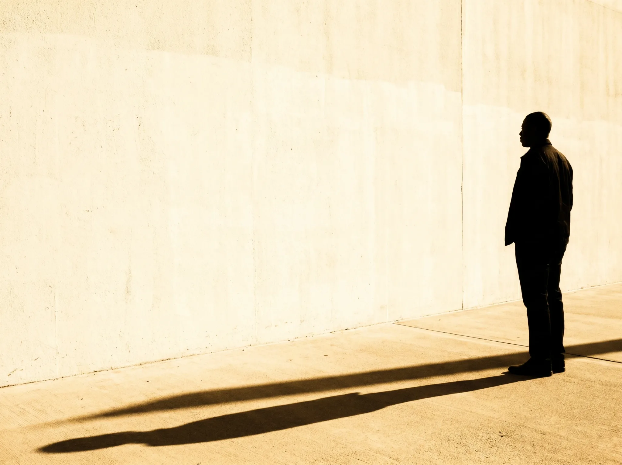Eine einzelne Silhouette mit langem Schatten an einer warmen Wand — du bist nicht falsch, nur in alten Mustern gefangen.
