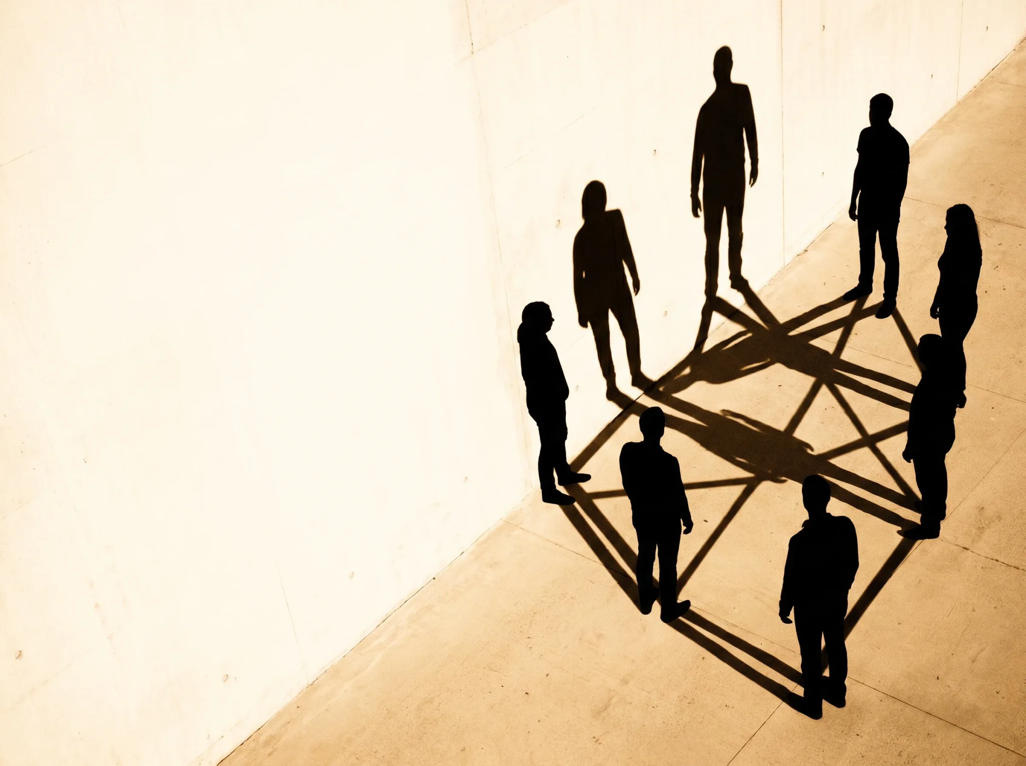 Mehrere Silhouetten, deren lange Schatten sich zu einem verbundenen Netz verweben — ein Team in Balance.